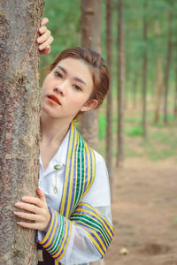 Portrait of young woman standing by tree trunk in forest