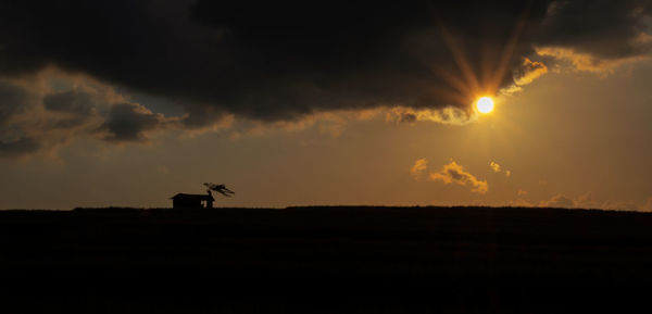 Silhouette airplane on field against sky during sunset