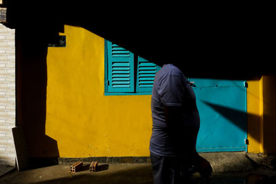 Rear view of man standing against yellow building