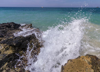 Waves splashing on rocks at sea shore against sky