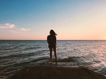 Rear view of silhouette woman standing on beach against clear sky