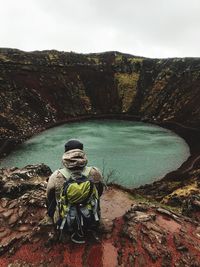 Rear view of man sitting on mountain by lake