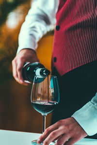 Midsection of man pouring wine in wineglass on table