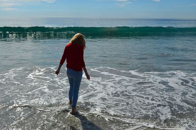 Rear view of woman standing on beach against sea