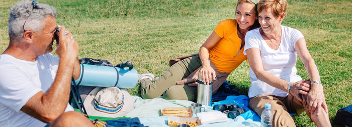 Senior father taking a photo to his family sitting on a blanket having picnic