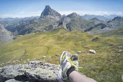 Low section of woman wearing shoes resting against mountains