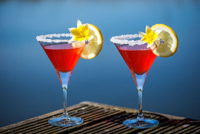 Drink garnished with yellow flower with lemon slice on wooden table against swimming pool