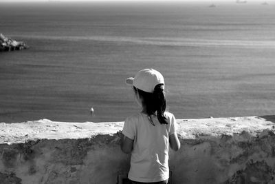 Rear view of girl standing by retaining wall against sea