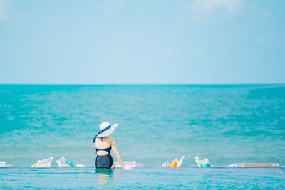 Rear view of woman sitting by swimming pool against sea