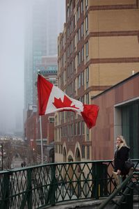 Woman standing by canadian flag against building during foggy weather