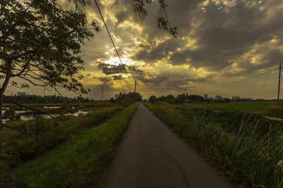 Road amidst field against sky during sunset