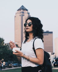 Woman having food while standing against buildings in city