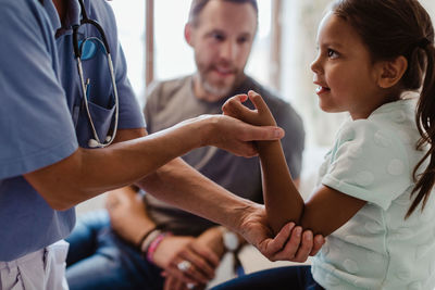 Midsection of nurse examining girl sitting with father at clinic