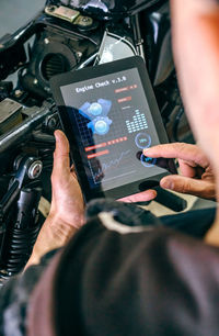 Midsection of man using digital tablet by motorcycle in garage