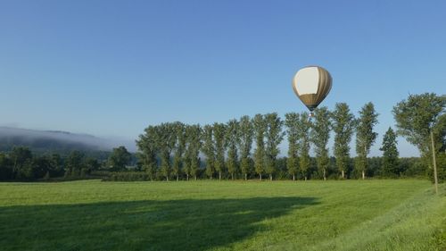 Hot air balloon flying over field against clear sky