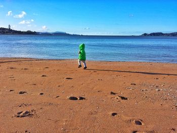 Rear view of boy on beach against sky