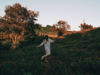 Rear view of woman with arms raised standing on field against clear sky