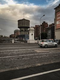 Cars on road by buildings against sky in city