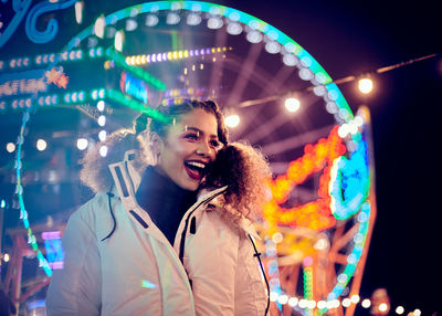 Happy woman standing against illuminated ferris wheel at night