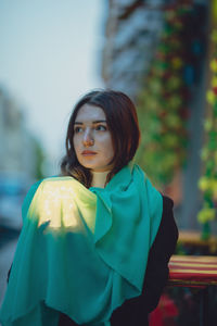 Thoughtful beautiful woman holding glowing jar under blue scarf in city at dusk