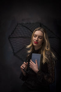 Portrait of young woman holding a book and a umbrella against black background