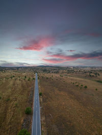 Road amidst field against sky during sunset