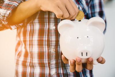 Midsection of man inserting coin in piggy bank