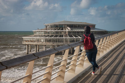 Rear view of woman standing by railing against sea