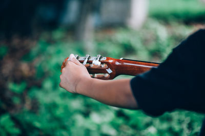 Cropped hand of person playing guitar over field