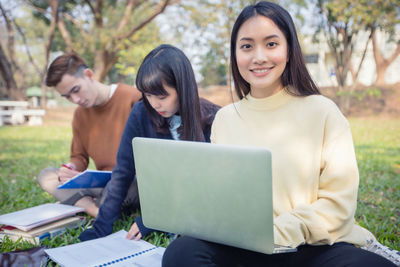Portrait of smiling young woman with friends using laptop on field