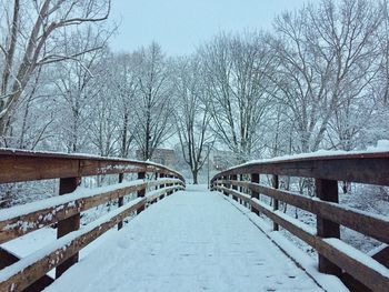 Snow covered footbridge against sky during winter