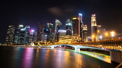 Illuminated bridge over river by buildings against sky at night