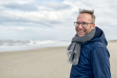 Portrait of smiling man standing at beach against sky