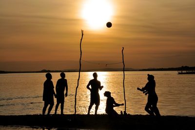 Silhouette people playing with ball on beach against sky during sunset