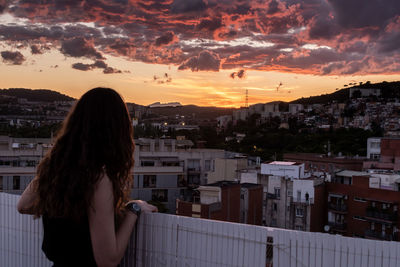 Woman standing by buildings against sky during sunset