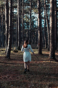 Rear view of woman standing by trees in forest