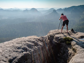 Man looking into viewfinder of his big camera, taking photo of amazing day in hilly landscape