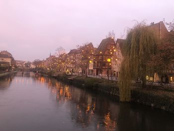 River by illuminated buildings against sky in city