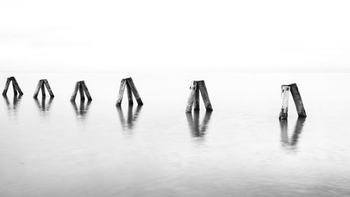 Wooden posts in sea against sky