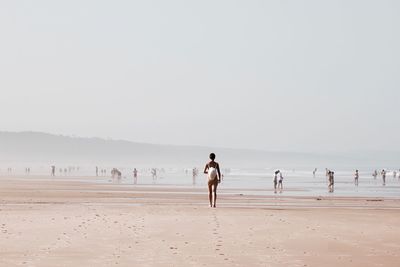 Rear view of woman walking at beach during foggy weather