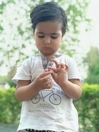 Cute boy holding small toy against trees