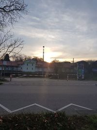 Road by buildings against sky during sunset in city