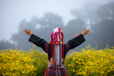 Woman in traditional clothing with arms outstretched standing against trees