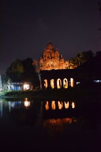 Illuminated building by lake against sky at night