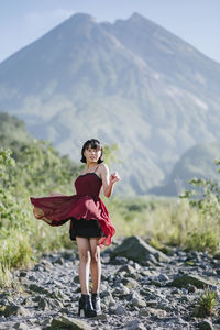 Full length portrait of woman standing on rocks against mountain