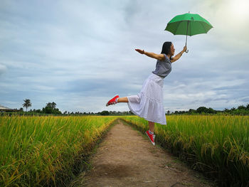 Woman jumping with umbrella over plants against sky