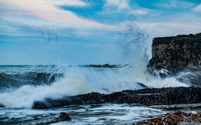 Waves splashing on rocks against sky