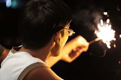 Side view of woman holding sparkler at night