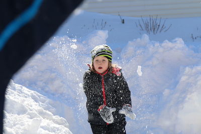 Cute girl wearing padded jacket and knit hat playing in snow