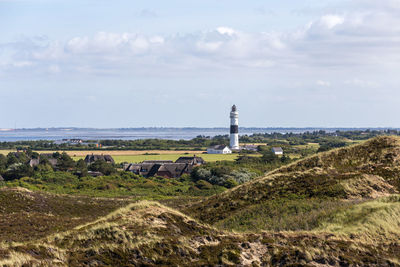 Lighthouse on field by sea against sky